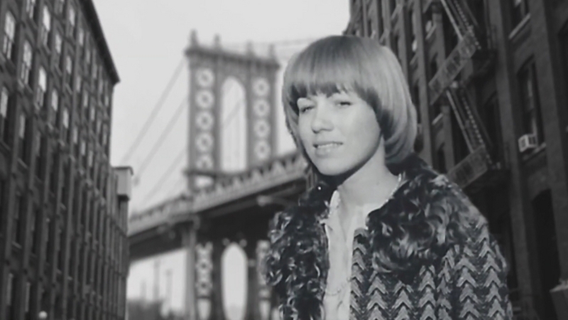 A young Barbara Corcoran stands on a New York City street with the Manhattan Bridge in the background