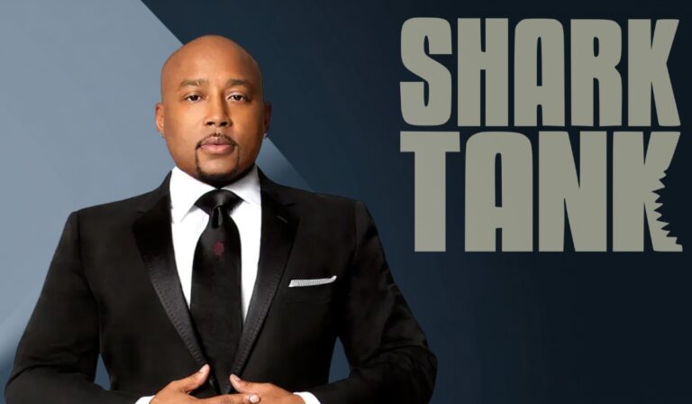 Man in a black suit standing confidently beside the Shark Tank logo
