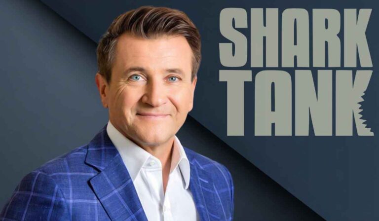 Man in a blue plaid suit standing in front of the Shark Tank logo