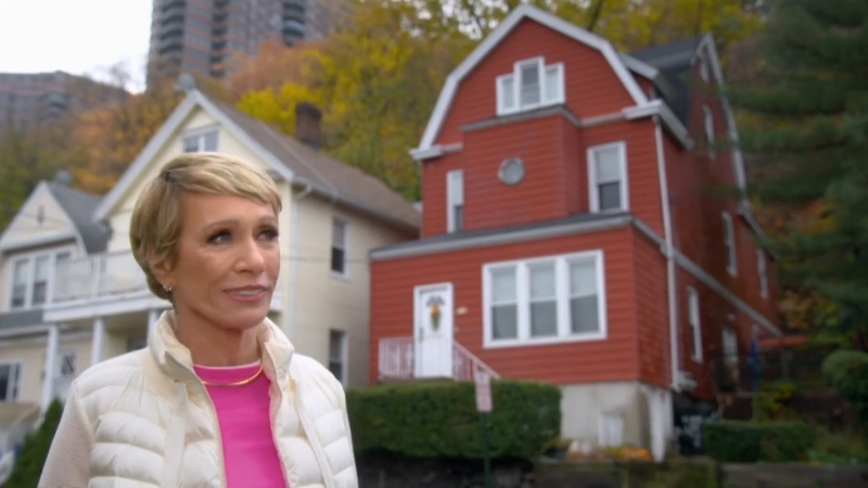 Barbara Corcoran stands in front of a red house