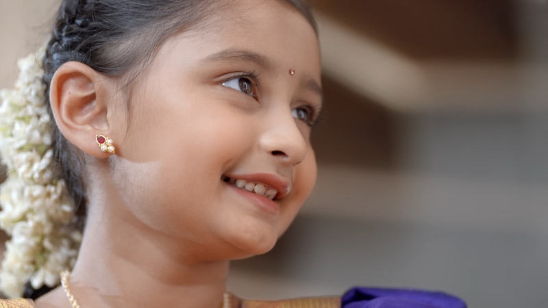 Myra Vaikul dressed in traditional Indian attire smiles softly, wearing jasmine flowers in her hair and gold earrings