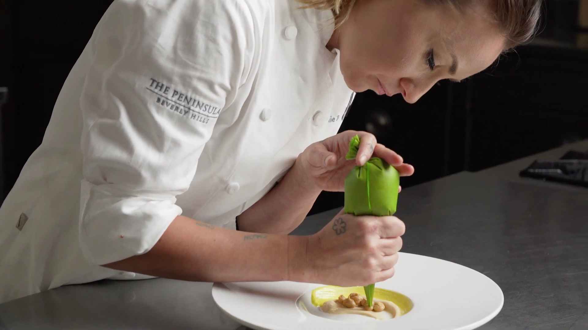 Stephanie Boswell piping sauce onto a gourmet dish while wearing a chef’s coat at The Peninsula Beverly Hills kitchen