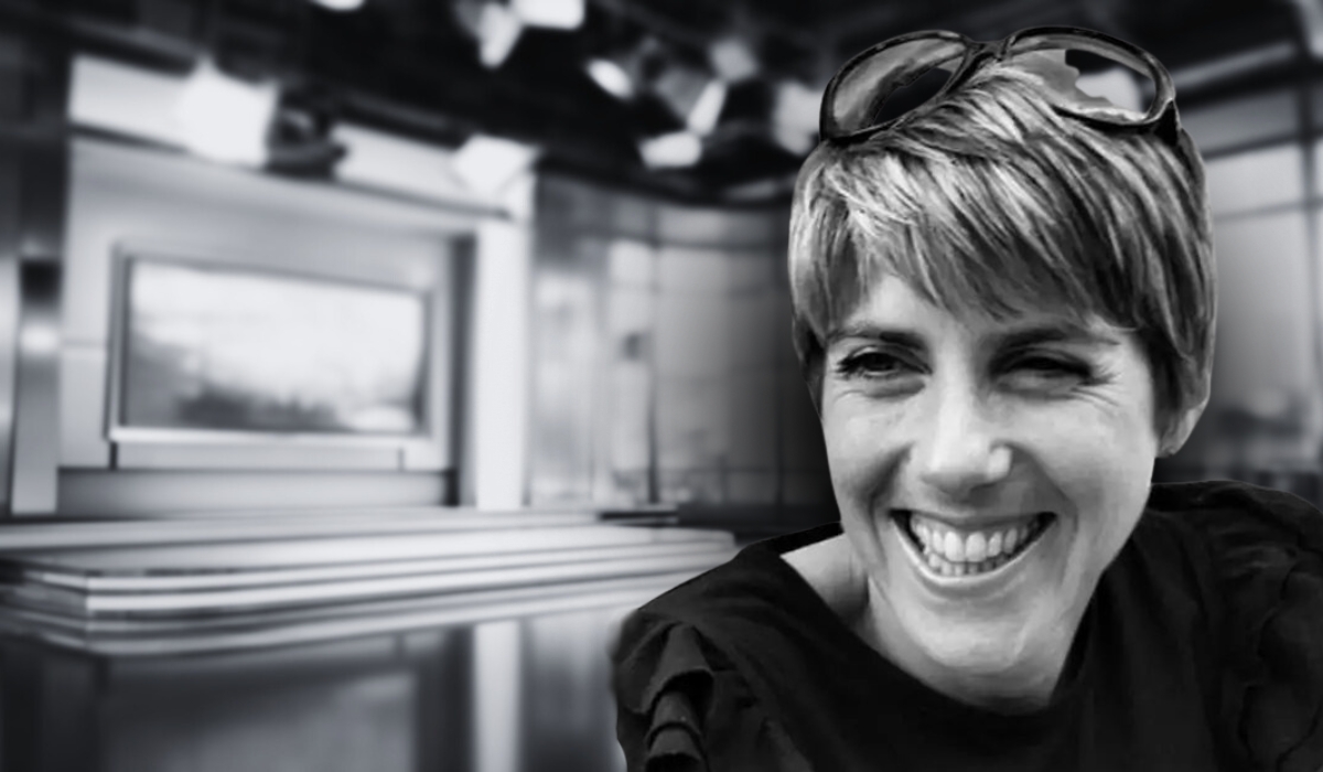 Black and white image of Judith Moritz smiling, with a blurred newsroom background