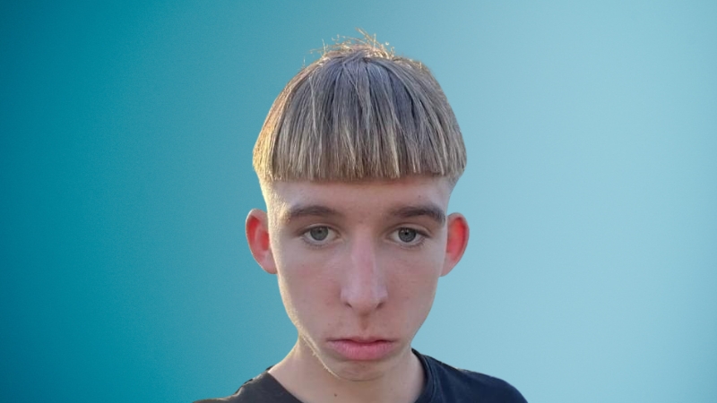 Lil Maceee with a bowl haircut and serious expression stands against a blue background