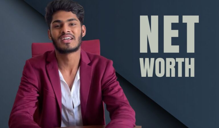 Man in maroon blazer sitting at a desk with the words “Net Worth” in the background