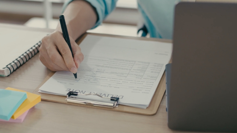 A person signs a delivery note beside a laptop