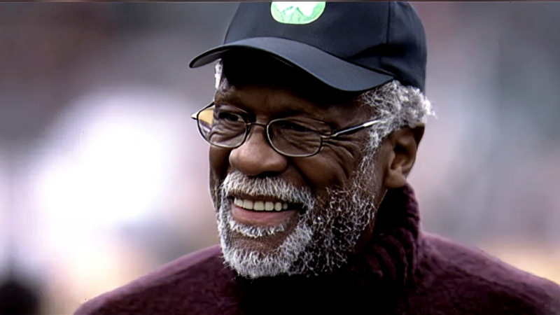 Bill Russell smiles in a casual moment, wearing glasses and a cap with the Celtics logo