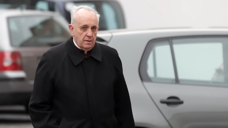 Pope Francis walking outdoors in a black coat