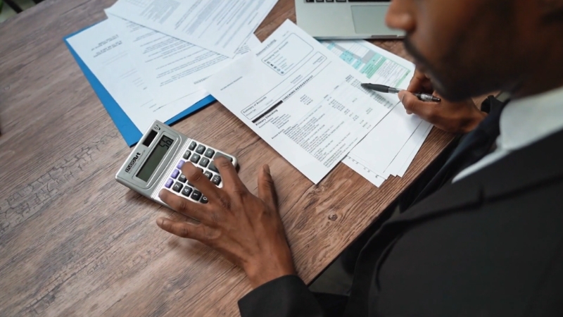 A person reviews tax documents with a calculator and laptop