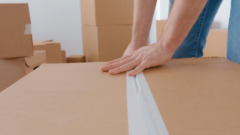 A person seals a cardboard box with tape during order preparation