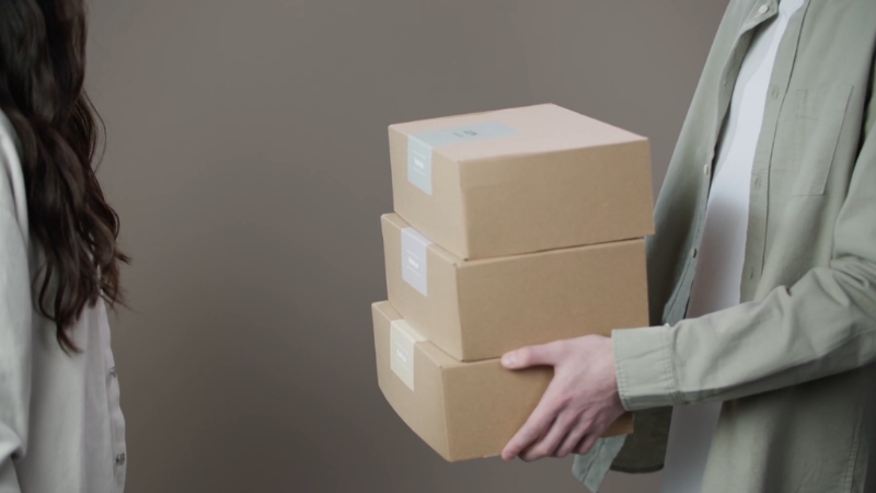 A person carries a stack of small cardboard shipping boxes