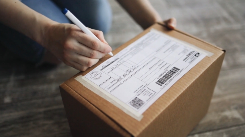 A person fills out a shipping label on a sealed cardboard box