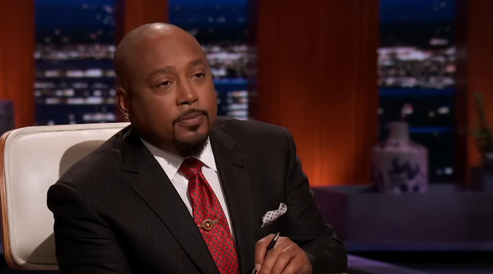 Daymond John seated on Shark Tank holding a notepad during a pitch