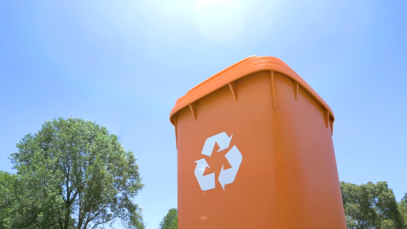 Orange recycling bin stands outdoors under a clear sky