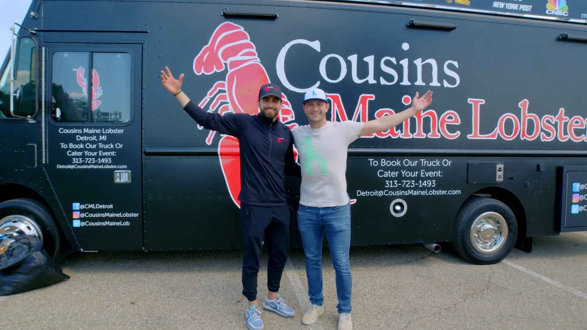 Two men standing with arms raised in front of a Cousins Maine Lobster food truck