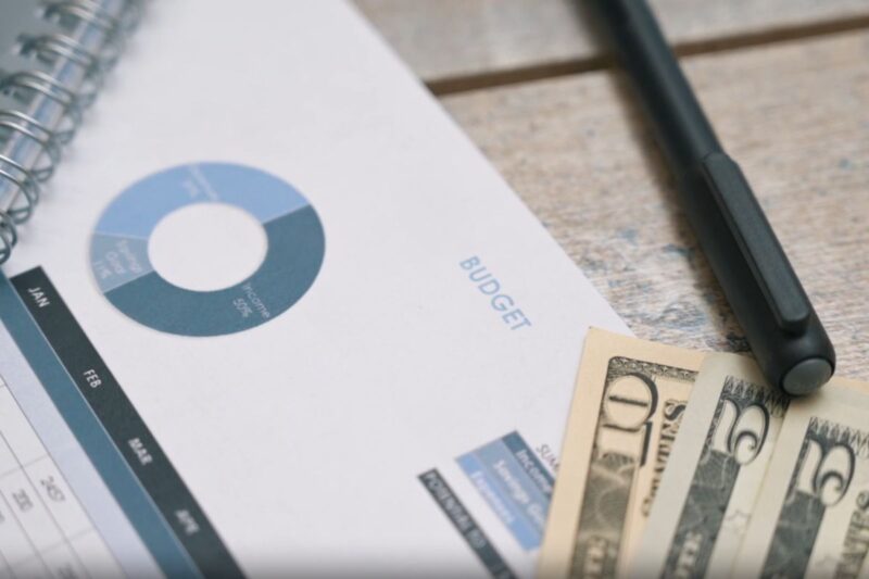 Financial report with budget chart, notebook, pen, and cash on a desk representing data strategy costs
