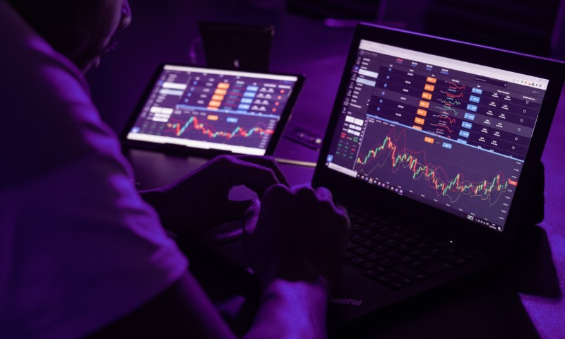 A person is analyzing stock market data on two screens in a dimly lit room
