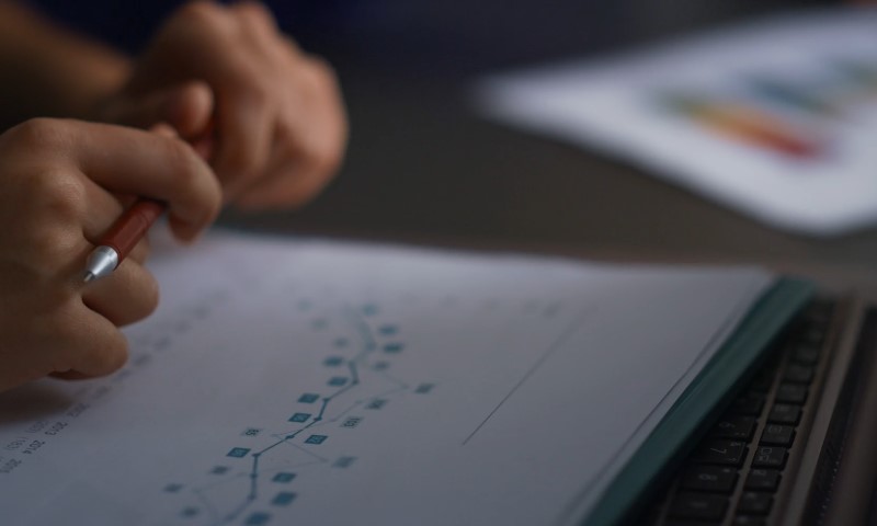 Hands holding a pencil over a piece of paper with a flowchart and keyboard nearby