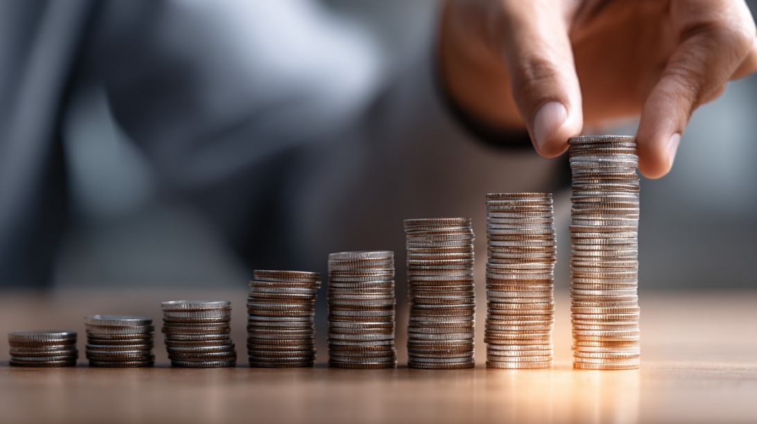 Hand placing coins on growing stacks symbolizing financial growth and investment planning