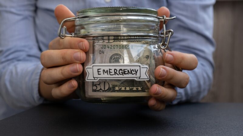 A person holds an emergency savings jar filled with cash for unexpected family expenses