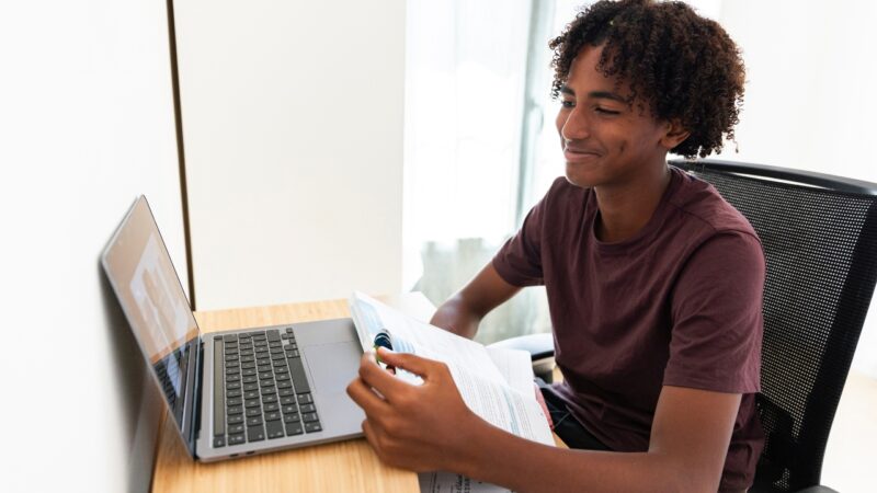 Student reviews printed material beside a laptop during an online class