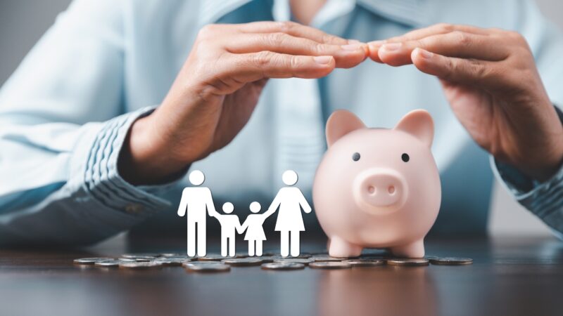 Hands protect a piggy bank and family icon to show family financial security