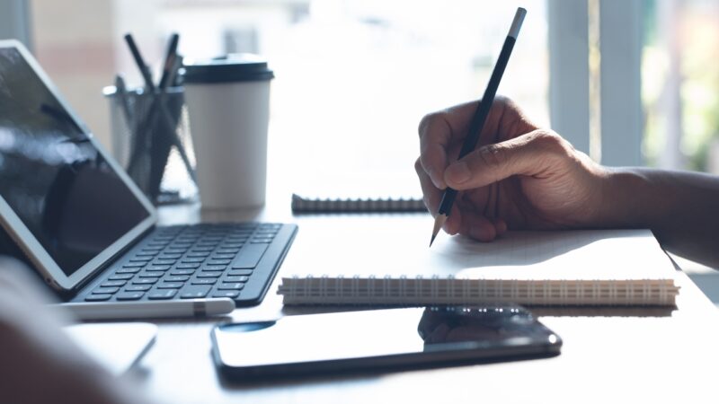 Person writes notes beside a tablet as part of a digital school workflow