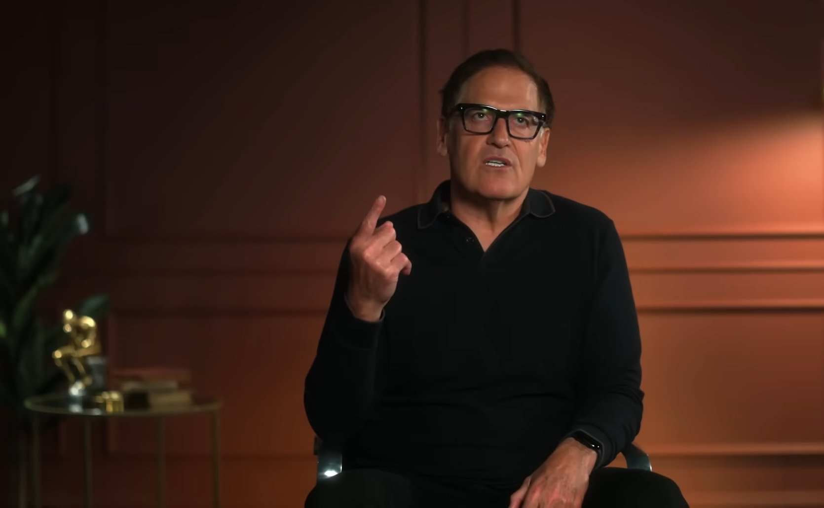 Businessman wearing glasses gestures while speaking in a studio.