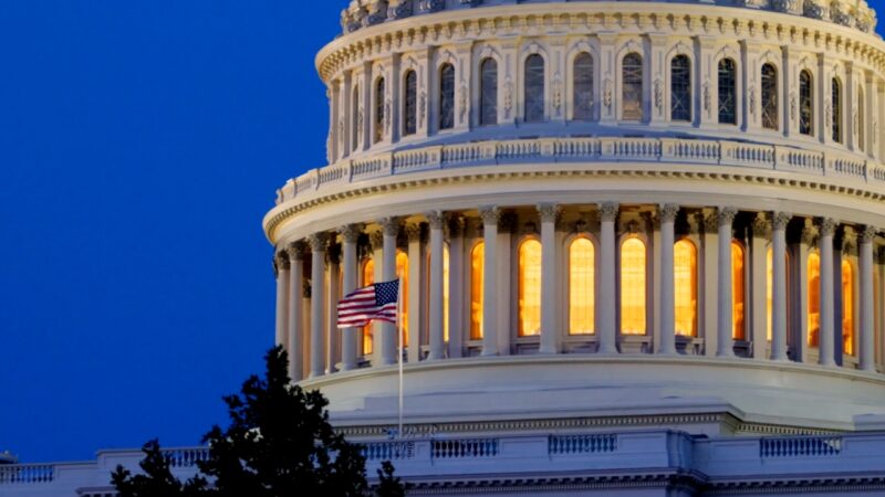 The U.S. Capitol dome glows at dusk beside an American flag